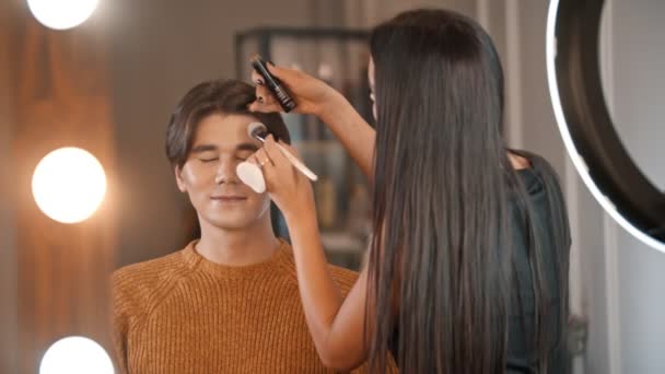 Woman make up artist applying cream contour on the face of male model using a brush — Stock Video