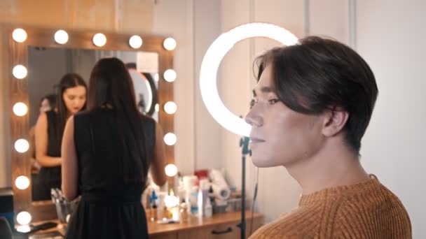 Mujer maquillaje artista aplicando reflejos en una cara de modelo masculino utilizando un cepillo — Vídeos de Stock