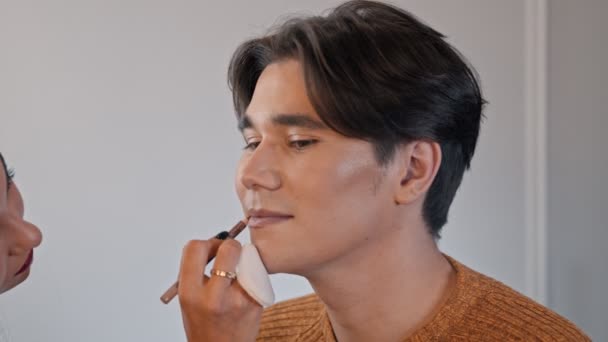Mujer maquillaje artista aplicando un lápiz desnudo en los labios de modelo masculino — Vídeos de Stock