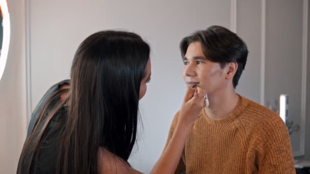 Woman make up artist applying a dark nude pencil on the lips of male model — Stock Video
