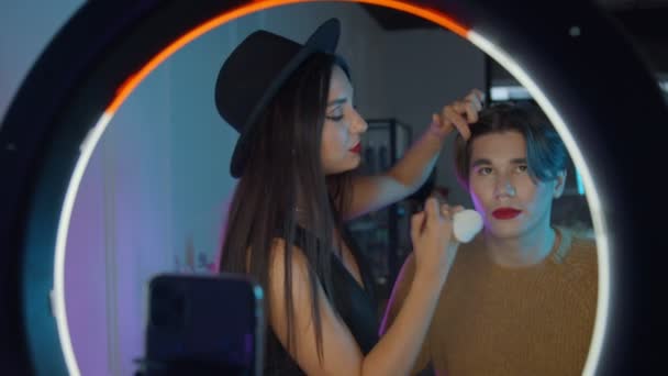Makeup studio - ung stilig man med djärvt rött läppstift och hans make up artist står framför en ring ljus - lägga sista handen — Stockvideo