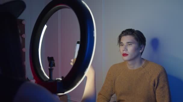 Mulher maquiadora tirando foto de seu modelo masculino com maquiagem em iluminação de néon - look ousado com lábios vermelhos — Vídeo de Stock