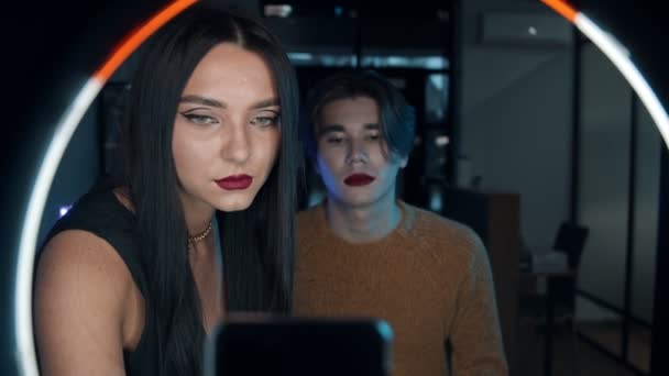 Make-up studio - jonge knappe man met gewaagde rode lippenstift en zijn vrouw make-up kunstenaar die voor een ring licht - het toevoegen van de finishing touch — Stockvideo