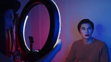 Makyaj stüdyosu - kadın ressam erkek modelinin neon ışıklı fotoğrafını çekiyor - kırmızı dudaklı ve ıslak saçlı cesur görünüm