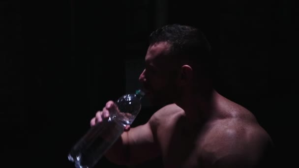 Sterke shirtloze man die water drinkt uit de plastic fles in het donker — Stockvideo