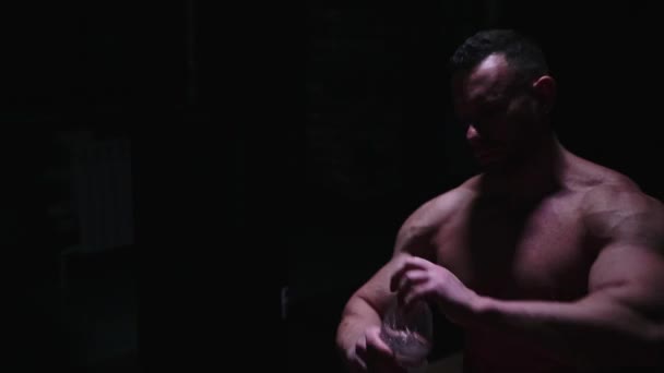 Hombre fuerte sin camisa bebiendo agua de la botella de plástico en el cuarto oscuro — Vídeos de Stock