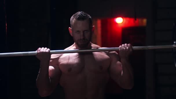 Homem sem camisa duro de pé no ginásio e fazendo exercícios - puxando um bar pesado com um esforço — Vídeo de Stock