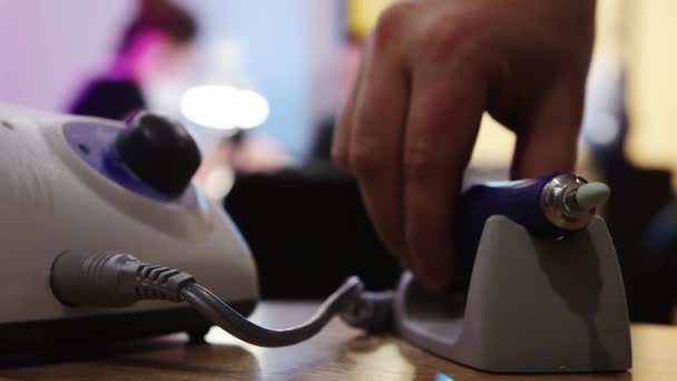 Аппаратный маникюр в маникюре - человек берет небольшой шлифовальный станок для ногтей со стола — стоковое видео