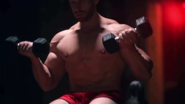 Tøff, stor mann som sitter i gymsalen og pumper hendene sine muskler med små dumbjeller - utstikkende årer – stockvideo