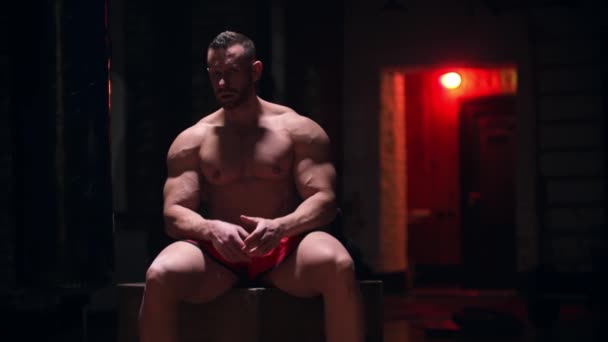 Жорсткий великий чоловік сидить у спортзалі з червоним контрастним освітленням — стокове відео