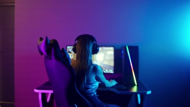 Junge blonde Spielerin sitzt in neonfarbenem Spielclub auf dem Stuhl — Stockvideo