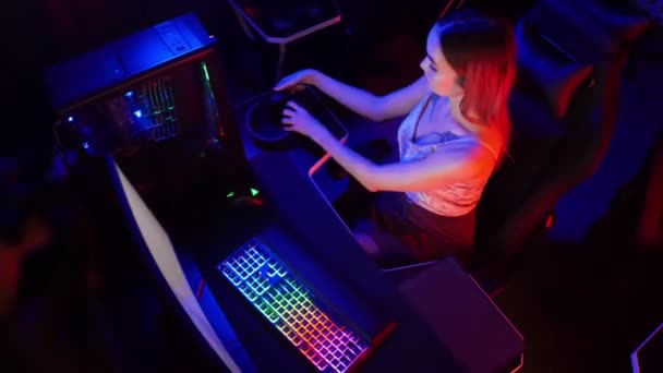 Jeune femme joueuse attrayante s'assoit sur la chaise dans le club de jeu au néon et jouer à des jeux — Video