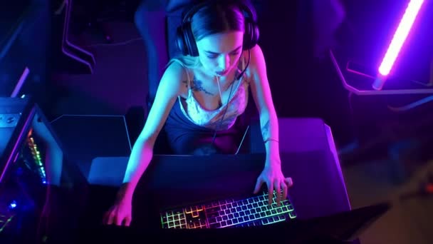 Concept de jeu - jeune femme joueuse attrayante s'assoit sur la chaise dans le club de jeu au néon et jouer à des jeux — Video