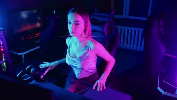 Концепция игры - молодая привлекательная девушка сидит в кресле в неоновом игровом клубе и высасывает леопарда — стоковое видео