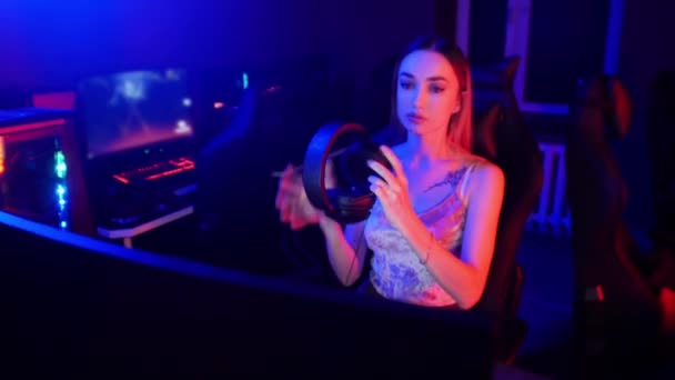 Concept de jeu - jeune femme joueuse attrayante s'assoit sur la chaise dans le club de jeu au néon et mettre de gros écouteurs — Video