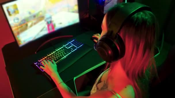 Gaming-Konzept - junge Gamer-Frau sitzt im Stuhl in Neon-Gaming-Club und spielt ein Online-Shooter-Spiel — Stockvideo