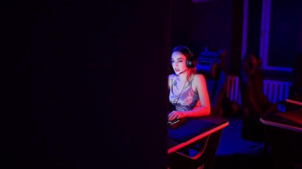 Conceito de jogo - jovem mulher atraente com tatuagens senta-se na cadeira no clube de jogos de néon e jogar um jogo online — Vídeo de Stock