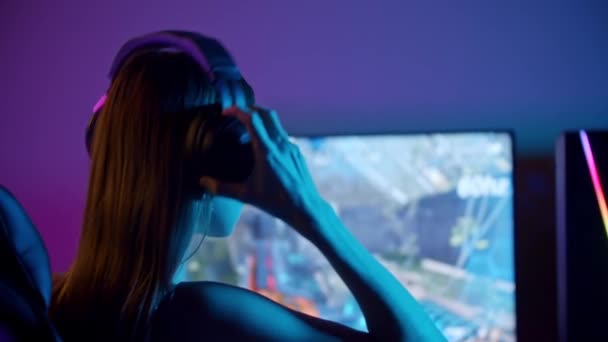 Junge Frau sitzt am PC - setzt Kopfhörer auf und beginnt zu spielen — Stockvideo