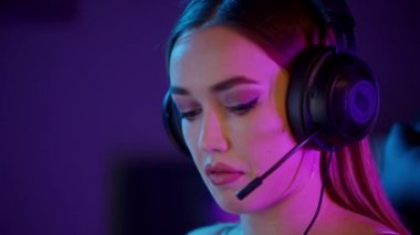 Dövmeli oyuncu kız sakız çiğniyor, bilgisayarın başında oturuyor ve online oyun oynuyor. Mikrofondaki diğer oyuncularla konuşuyor.