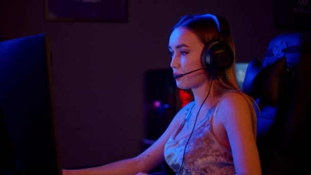 Fille joueuse tatouée dans de gros écouteurs assis près du PC dans le club de jeu au néon et jouer à un jeu en ligne — Video