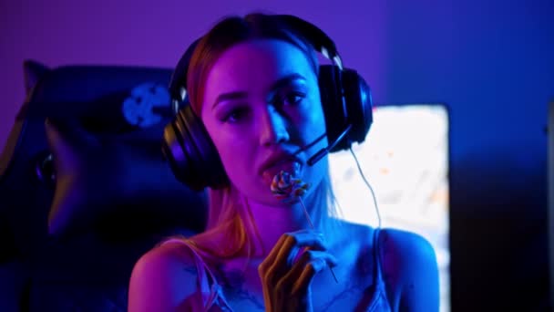 Татуированная девушка-геймер сидит у игрового ПК и сосет леденец — стоковое видео