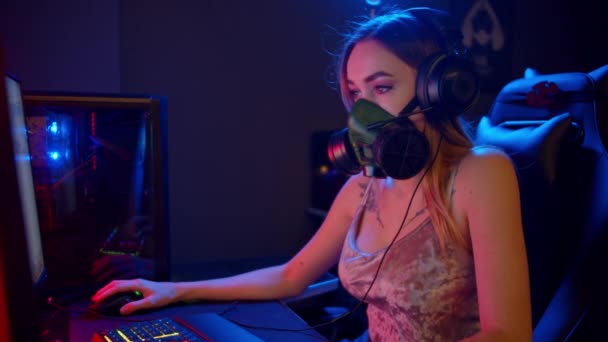 Jeune joueuse dans un respirateur noir assis près du PC et jouant à un jeu — Video