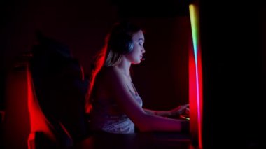 Seksi dövmeli genç kadın neon oyun kulübünde oturuyor ve oyun oynuyor. Gülümsüyor ve kameraya bakıyor.