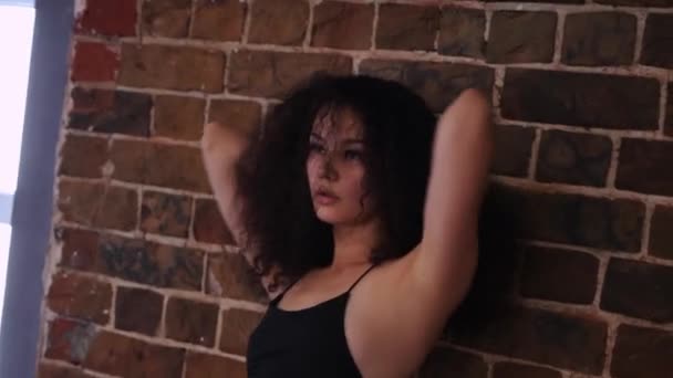 Jeune femme attrayante avec des cheveux bouclés dansant par le mur de briques orange — Video