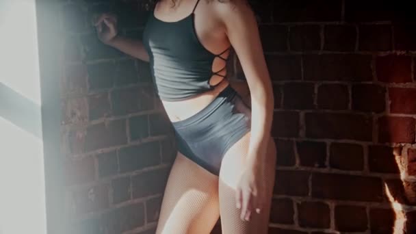 Strip bailando en el estudio - mujer rizada atractiva joven en traje diminuto negro baile sexy por la pared de ladrillo naranja — Vídeos de Stock