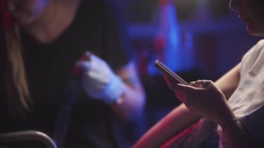 Dövme oturumu - koltukta oturan bir müşteri telefonunu kontrol ediyor