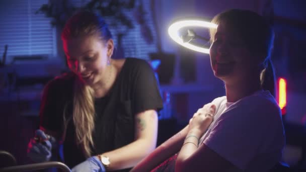 Sesja tatuażowa - młoda kobieta robi sobie tatuaż na ramieniu - śmieje się i patrzy w kamerę — Wideo stockowe