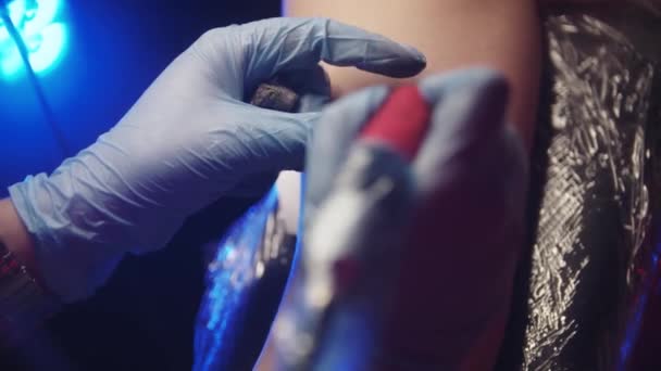 Sesja tatuażowa - kobieta robi sobie czarny i czerwony abstrakcyjny tatuaż twarzy na ramieniu — Wideo stockowe