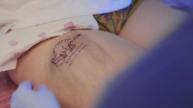 Kalçasında Rusça sözcüklerle dinozor dövmesi yaptıran bir kadın.