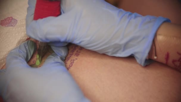 En kvinna får en grön dinosaurie tatuering med ryska ord i blått bläck — Stockvideo