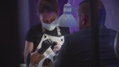 Erkek manikür seansı - siyah eldivenli kadın usta tırnak törpüsüyle tırnak testeresi