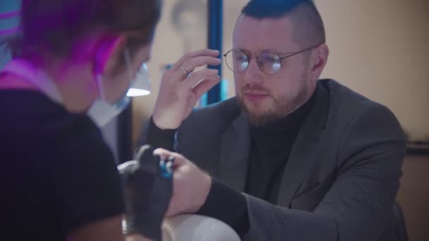 Чоловічий манікюр - бізнесмен, що сидить на манікюрній сесії в салоні, розмовляє з господарем і знімає окуляри — стокове відео
