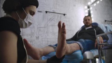 Pedikür prosedürü. Usta, erkek müşterisinin topuğundaki sert deriyi parlatır.