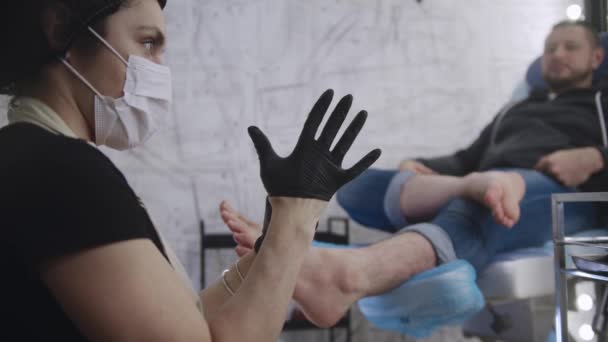 A man having a pedicure procedure - the master putting on a black glove — Stock Video