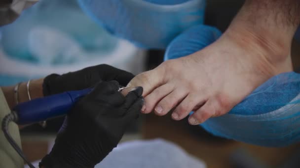 Procedimiento de pedicura - el maestro moliendo las uñas de los pies de su cliente masculino usando una pequeña máquina de perforación — Vídeo de stock