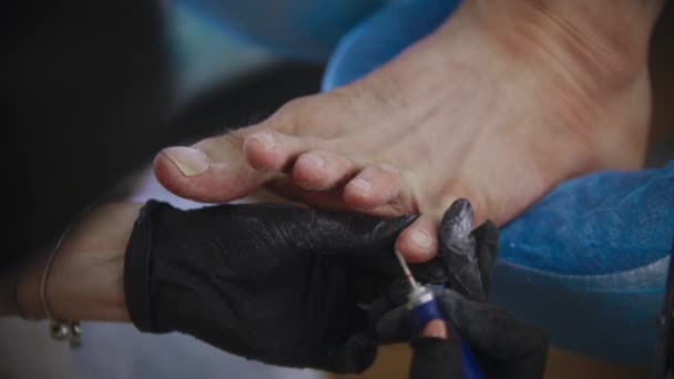Pedikúra mistr broušení a čištění pokožky nehtů na nohou svého klienta pomocí vrtačky — Stock video
