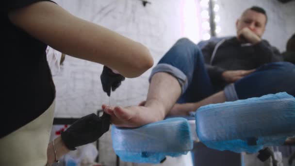 Pedicure procedure - de meester in zwarte handschoenen doet de teennagels van haar mannelijke cliënt met behulp van een nagelvijl — Stockvideo