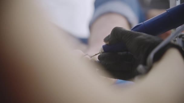 Die Pediküre-Meisterin reinigt mit einem kleinen Bohrgerät die Nagelplatte der Fußnägel ihres männlichen Kunden — Stockvideo
