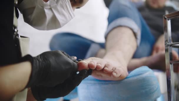 Die Pediküre-Meisterin schneidet die Fußnägel ihres männlichen Kunden mit einem Nagelschere — Stockvideo