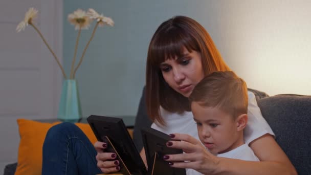 Lycklig familj - kvinna med sin lille son sitter på en soffa och tittar på fotografierna sedan tittar i kameran — Stockvideo