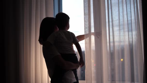 Madre sosteniendo a su hijo y mirando a las calles detrás de la ventana — Vídeos de Stock