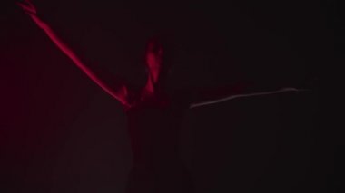 Siyah elbiseli zarif kadın balerin kırmızı ışıkta parmak uçlarında dans ediyor.