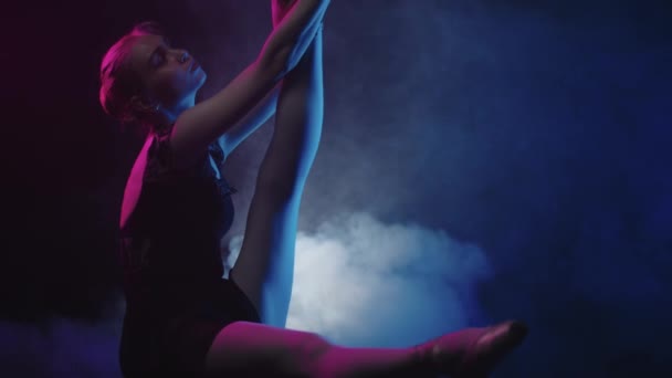 Tânără femeie balerină stă pe podea în studio negru afumat și face stretching — Videoclip de stoc