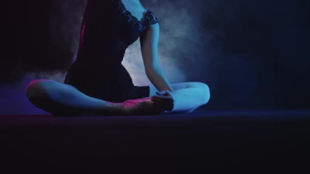 Genç bayan balerin dumanlı stüdyoda yerde oturuyor ve esneme hareketleri yapıyor. — Stok video