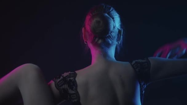 Mujer joven bailarina calentándose en el estudio negro de pie de nuevo a la cámara — Vídeos de Stock