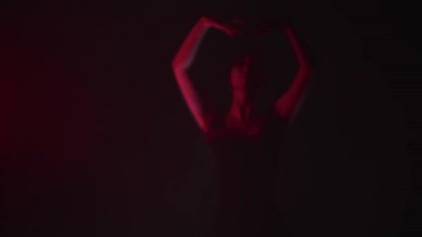 Молодая балерина в черном платье изящно медленно танцует при красном освещении — стоковое видео